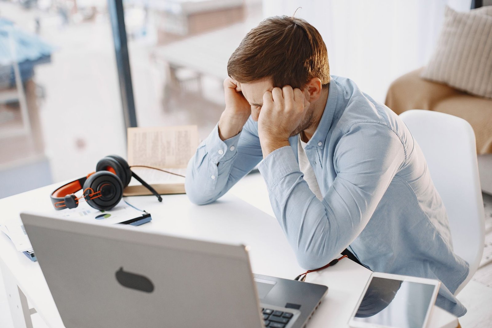 Man in a home office looks frustrated while working. He sits at a desk with a laptop and headphones.